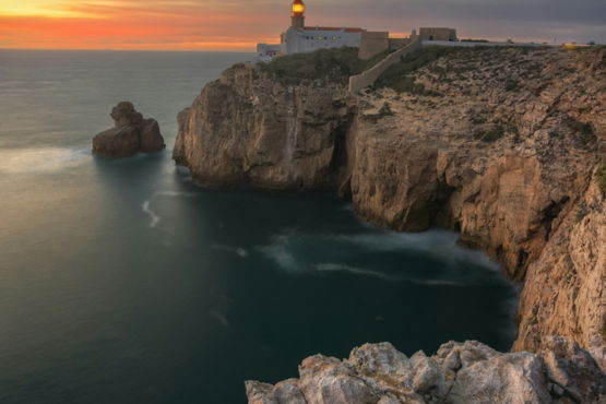 Lighthouse on a cliff overlooking the ocean at sunset